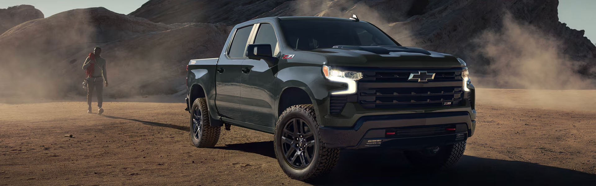 2026 Chevrolet Silverado 1500 pickup truck driving off-road in a rugged desert landscape with rocky terrain and dust in the background.