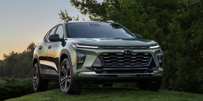 2026 Chevrolet Trax green SUV parked in a garden surrounded by trees, highlighting its bold design, modern styling, and compact versatility.