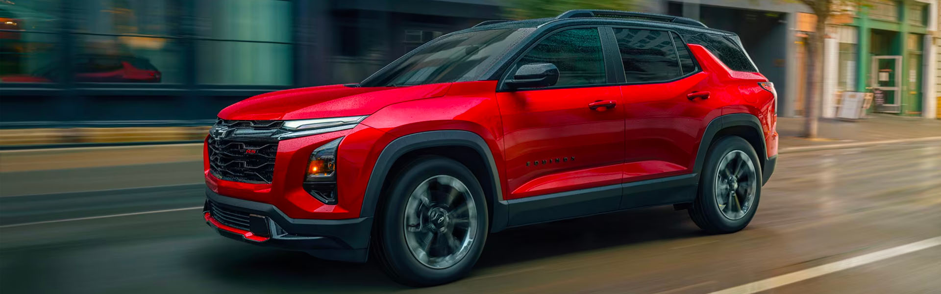 Red 2026 Chevrolet Equinox driving on a city street, showcasing a modern SUV design with sleek lines.