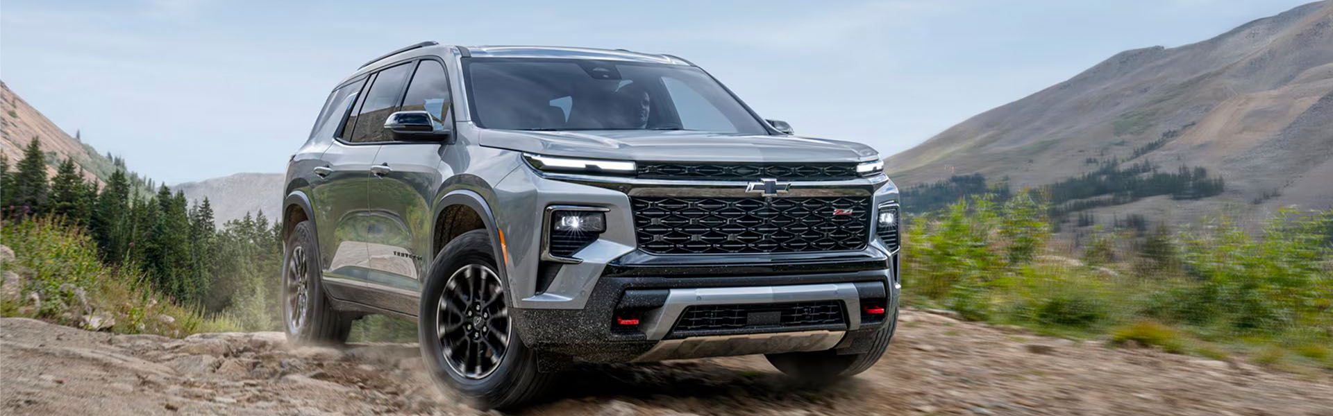 2026 Chevrolet Traverse driving on a rugged terrain with mountains in the background.
