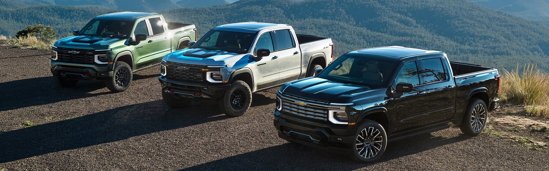 Three 2027 Chevrolet Silverado 1500 parked near mountain landscape showcasing its modern features.