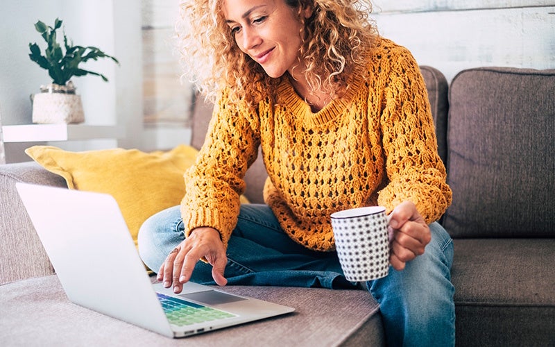 Woman sitting on the couch with a mug in hand, using a computer