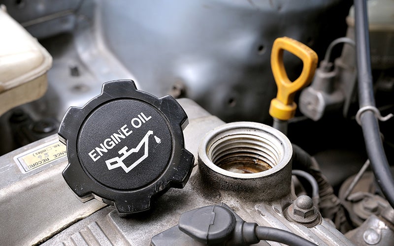 Unscrewed oil cap sitting on the engine of a car. The cap reads 'Enging Oil'